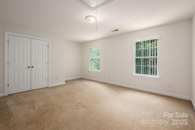 unfurnished bedroom with baseboards, multiple windows, attic access, and visible vents
