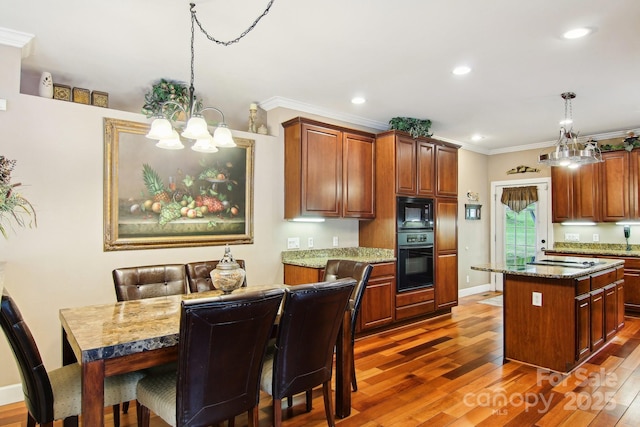 kitchen with ornamental molding, wood finished floors, a center island, black appliances, and a notable chandelier