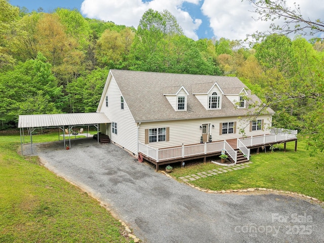 new england style home with a wooded view, gravel driveway, a deck, and a front yard
