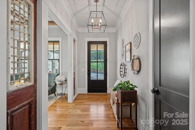 entryway featuring light wood-style floors, baseboards, ornamental molding, and an inviting chandelier