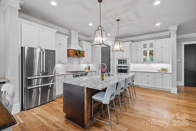 kitchen with stainless steel appliances, a sink, crown molding, white cabinetry, and custom range hood
