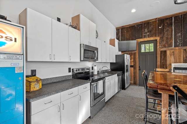 kitchen featuring dark countertops, a sink, wooden walls, white cabinets, and appliances with stainless steel finishes