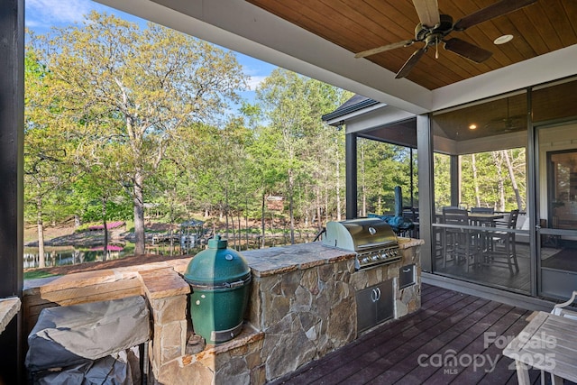 wooden terrace featuring grilling area, an outdoor kitchen, and a ceiling fan