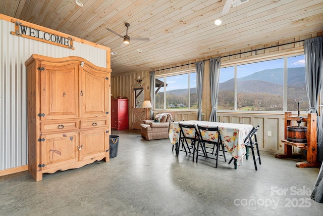 dining area with concrete floors, a mountain view, a ceiling fan, and wooden ceiling