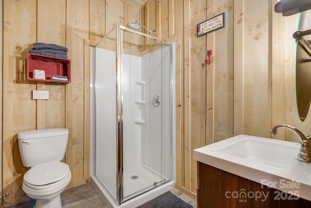bathroom with vanity, toilet, a stall shower, and wood walls