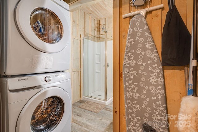 washroom with stacked washing maching and dryer, wood finished floors, and laundry area