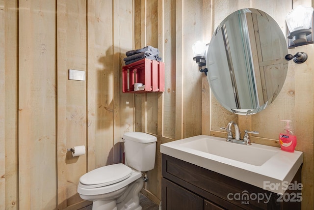 half bath with toilet, vanity, and wooden walls