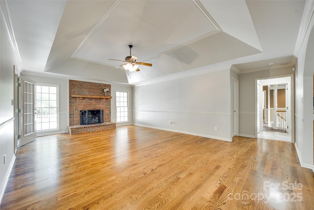 unfurnished living room with a raised ceiling, ceiling fan, light wood finished floors, a fireplace, and crown molding