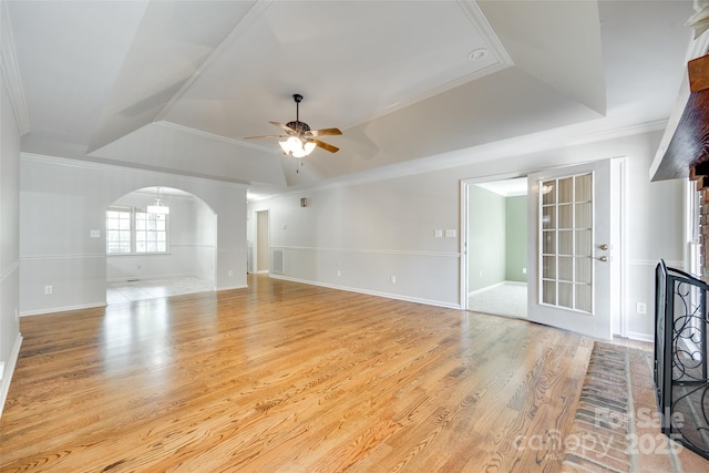 unfurnished living room featuring a tray ceiling, a ceiling fan, light wood-style flooring, crown molding, and arched walkways