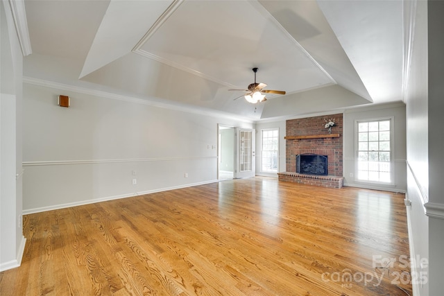 unfurnished living room featuring a raised ceiling, a ceiling fan, ornamental molding, a fireplace, and wood finished floors