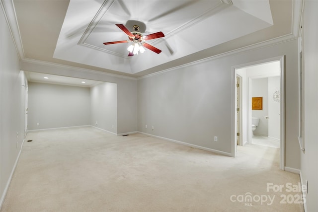 empty room featuring a raised ceiling, ceiling fan, ornamental molding, light colored carpet, and baseboards