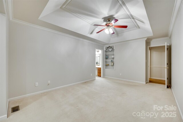 spare room with a raised ceiling, ceiling fan, carpet flooring, crown molding, and baseboards