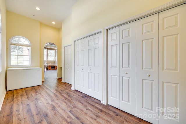 unfurnished bedroom featuring arched walkways, wood finished floors, multiple closets, and recessed lighting