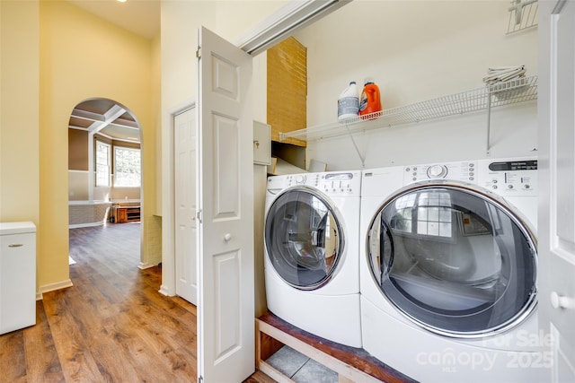 laundry area featuring independent washer and dryer, arched walkways, and wood finished floors