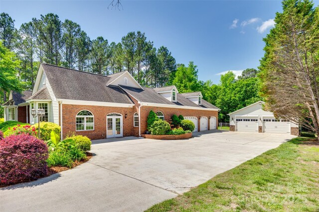 view of front of home with brick siding, french doors, concrete driveway, and roof with shingles