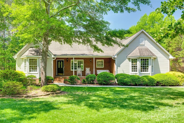 view of front facade with a front lawn, brick siding, roof with shingles, and covered porch