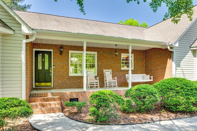 view of exterior entry with covered porch, roof with shingles, and brick siding