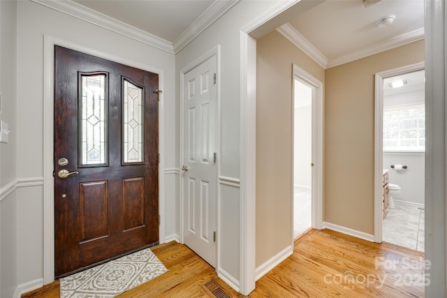 foyer entrance with light wood finished floors, crown molding, and baseboards