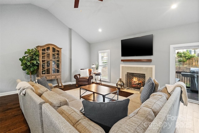 living room featuring vaulted ceiling, a tile fireplace, a ceiling fan, and wood finished floors