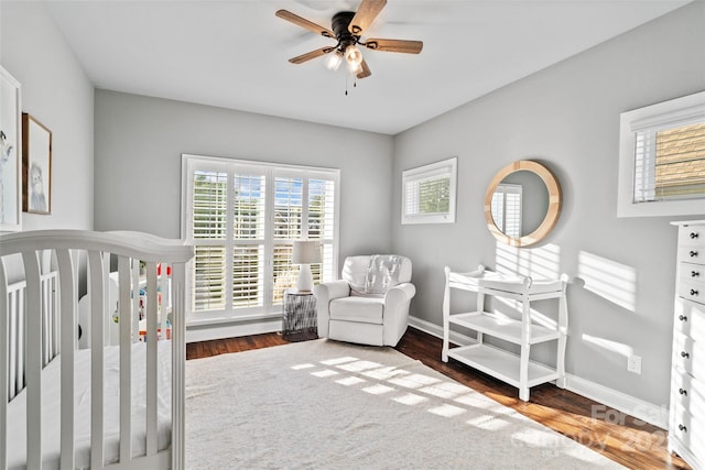 bedroom featuring baseboards, a ceiling fan, wood finished floors, and a nursery area