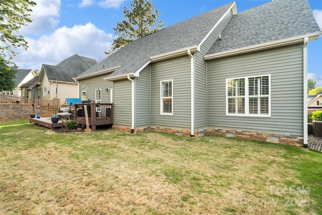 back of property with a yard, roof with shingles, and a deck