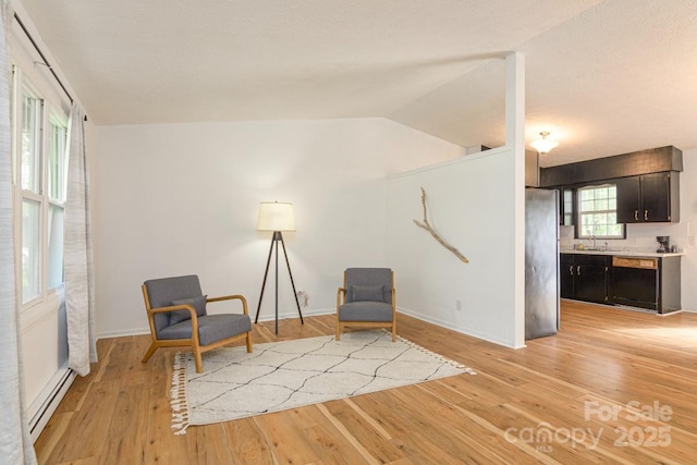 sitting room with a baseboard radiator, light wood finished floors, vaulted ceiling, and baseboards