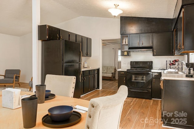 kitchen featuring a sink, under cabinet range hood, light wood-style floors, black appliances, and lofted ceiling