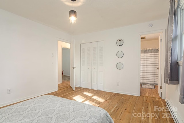 bedroom with a baseboard radiator, a closet, baseboards, light wood-type flooring, and ensuite bath