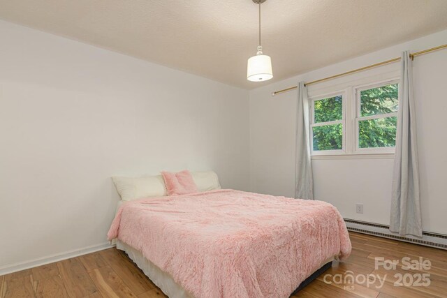 bedroom with baseboards, wood finished floors, and a baseboard radiator