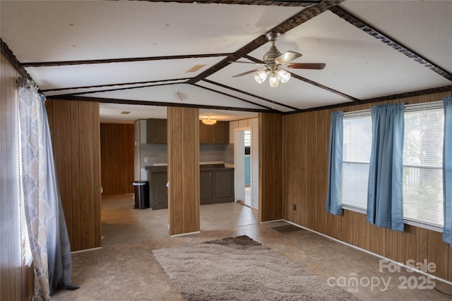 empty room with wood walls, vaulted ceiling with beams, and ceiling fan