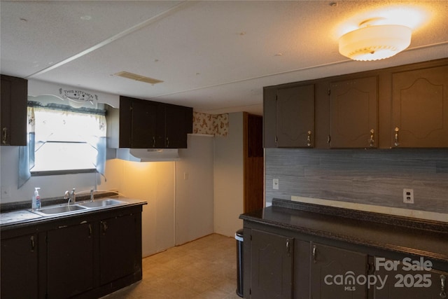 kitchen with a sink, dark countertops, visible vents, backsplash, and light floors