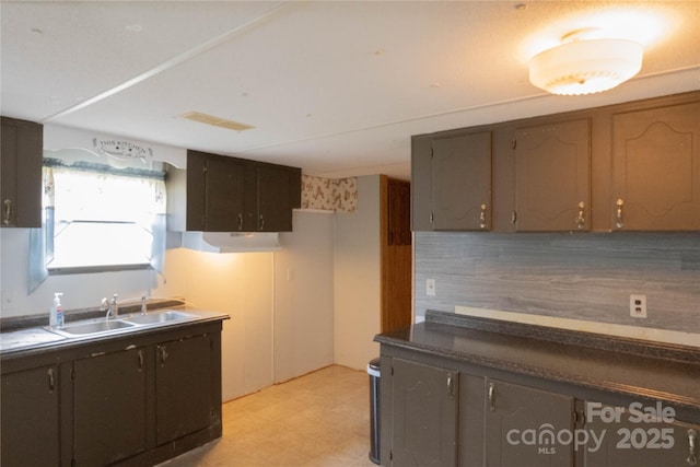 kitchen with a sink, tasteful backsplash, dark countertops, visible vents, and light floors