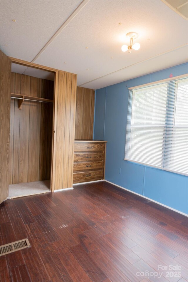 unfurnished bedroom featuring baseboards, visible vents, wood walls, wood finished floors, and a closet