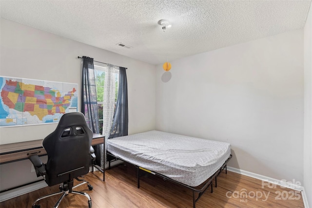 bedroom with wood finished floors, visible vents, and a textured ceiling