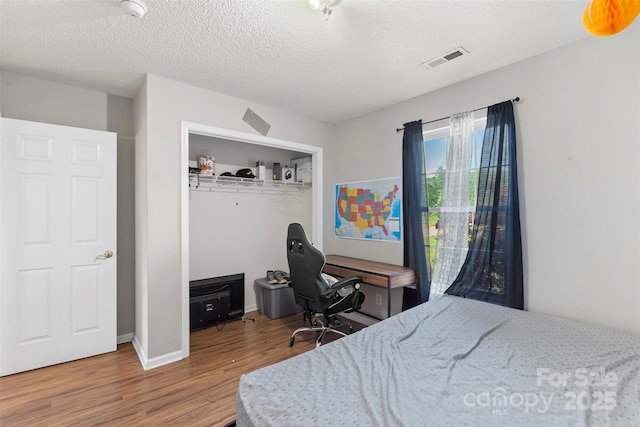 bedroom featuring a textured ceiling, baseboards, visible vents, wood finished floors, and a closet