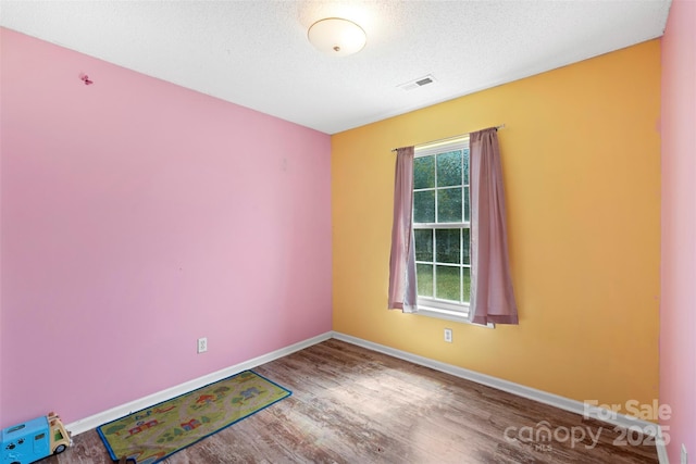 spare room featuring visible vents, plenty of natural light, baseboards, and wood finished floors