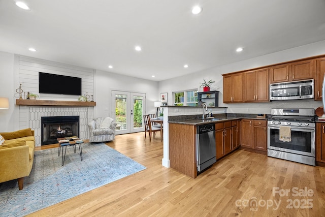 kitchen with appliances with stainless steel finishes, brown cabinets, a sink, light wood finished floors, and open floor plan