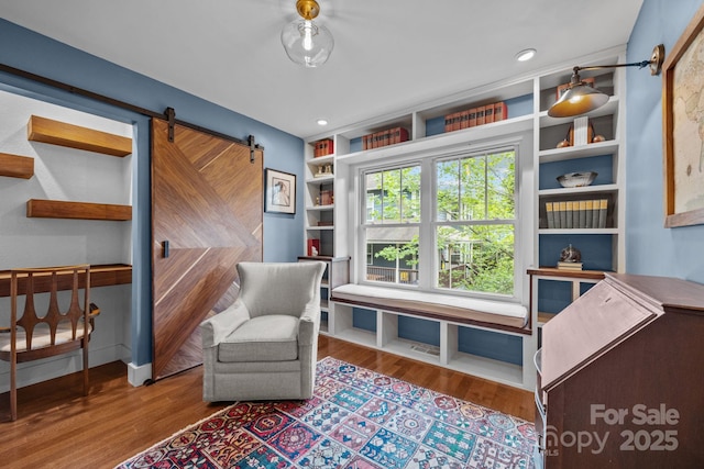 sitting room featuring a barn door, built in features, and wood finished floors