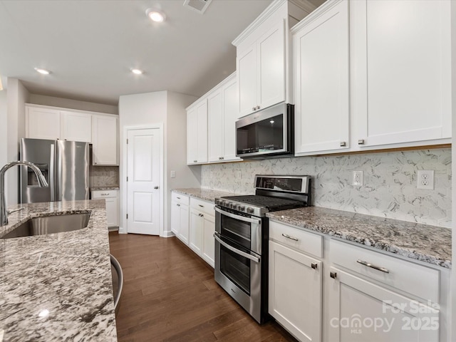kitchen with a sink, decorative backsplash, white cabinets, appliances with stainless steel finishes, and dark wood-type flooring