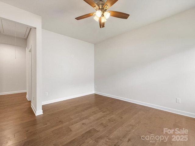 spare room featuring attic access, baseboards, wood finished floors, and a ceiling fan