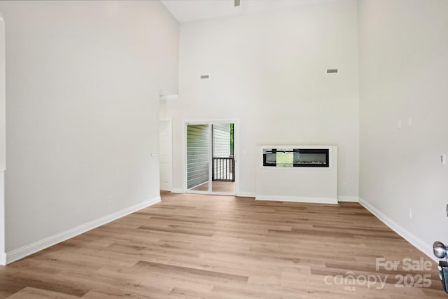 unfurnished living room featuring a glass covered fireplace, baseboards, light wood finished floors, and high vaulted ceiling