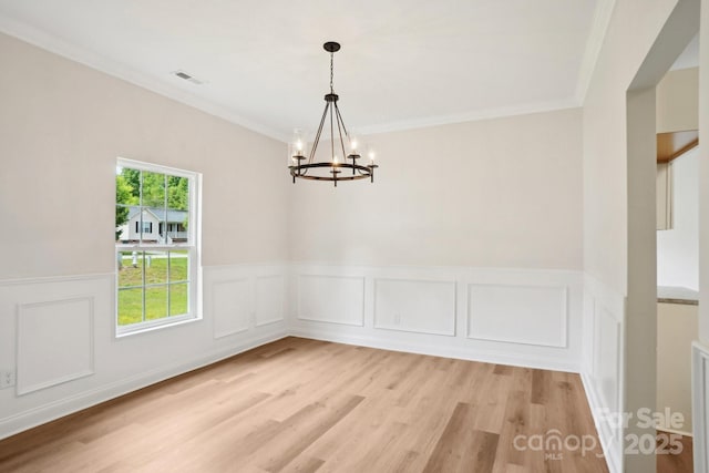 unfurnished room with light wood-style flooring, visible vents, a wainscoted wall, and an inviting chandelier