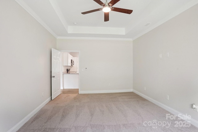 unfurnished room featuring crown molding, a ceiling fan, a tray ceiling, light colored carpet, and baseboards