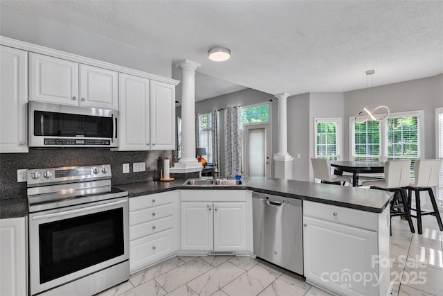 5775 Monticello Dr NW, Concord, NC 28027 - kitchen featuring decorative columns, appliances with stainless steel finishes, dark countertops, a sink, and a peninsula