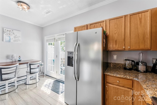 8814 Gerren Ct, Charlotte, NC 28217 - kitchen featuring crown molding, stainless steel fridge, brown cabinetry, dark stone countertops, and visible vents