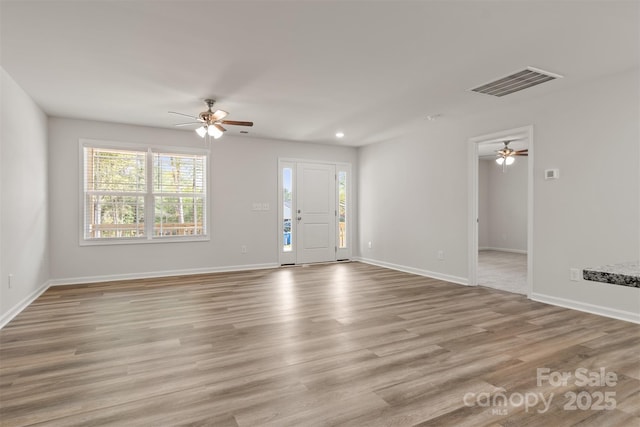 unfurnished living room featuring a wealth of natural light, a ceiling fan, wood finished floors, and visible vents