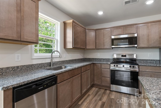kitchen featuring dark wood-style flooring, appliances with stainless steel finishes, a sink, dark stone counters, and visible vents