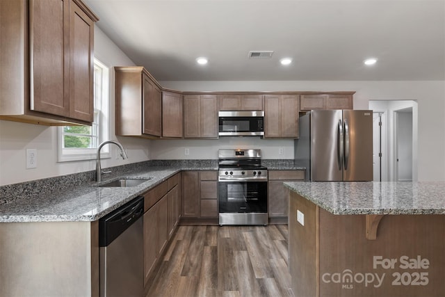 kitchen featuring visible vents, appliances with stainless steel finishes, dark wood finished floors, a sink, and light stone counters