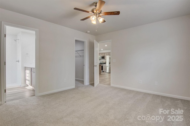 unfurnished bedroom featuring freestanding refrigerator, light carpet, baseboards, a walk in closet, and connected bathroom