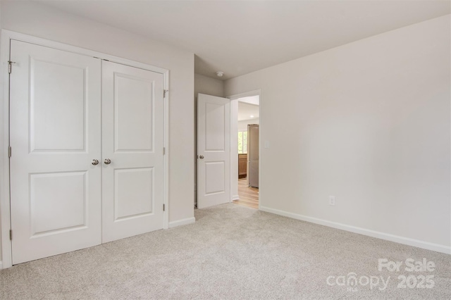 unfurnished bedroom with baseboards, light colored carpet, and a closet